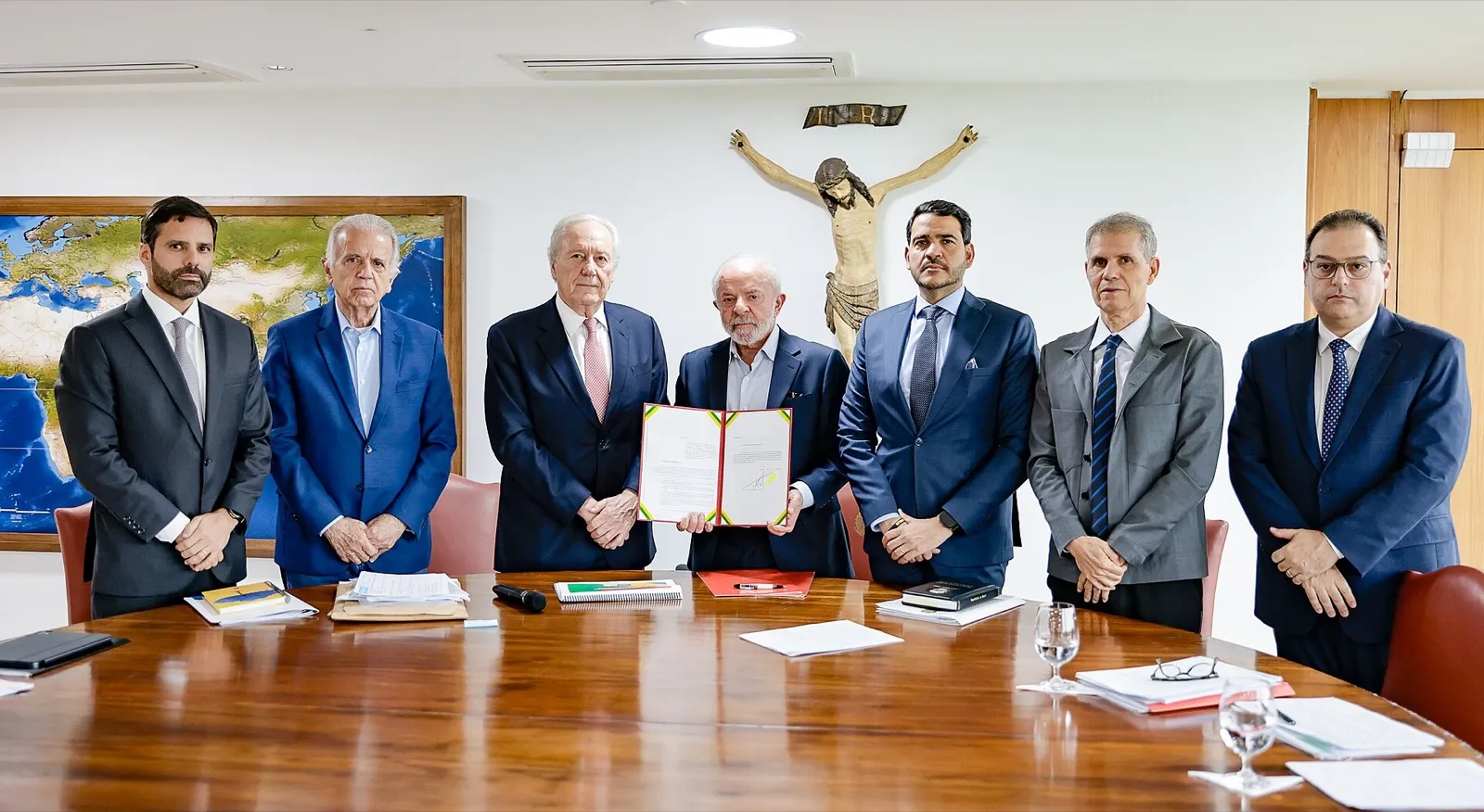 Lula segura o documento assinado, cercado por ministros e autoridades em torno de uma mesa no Palácio do Planalto.