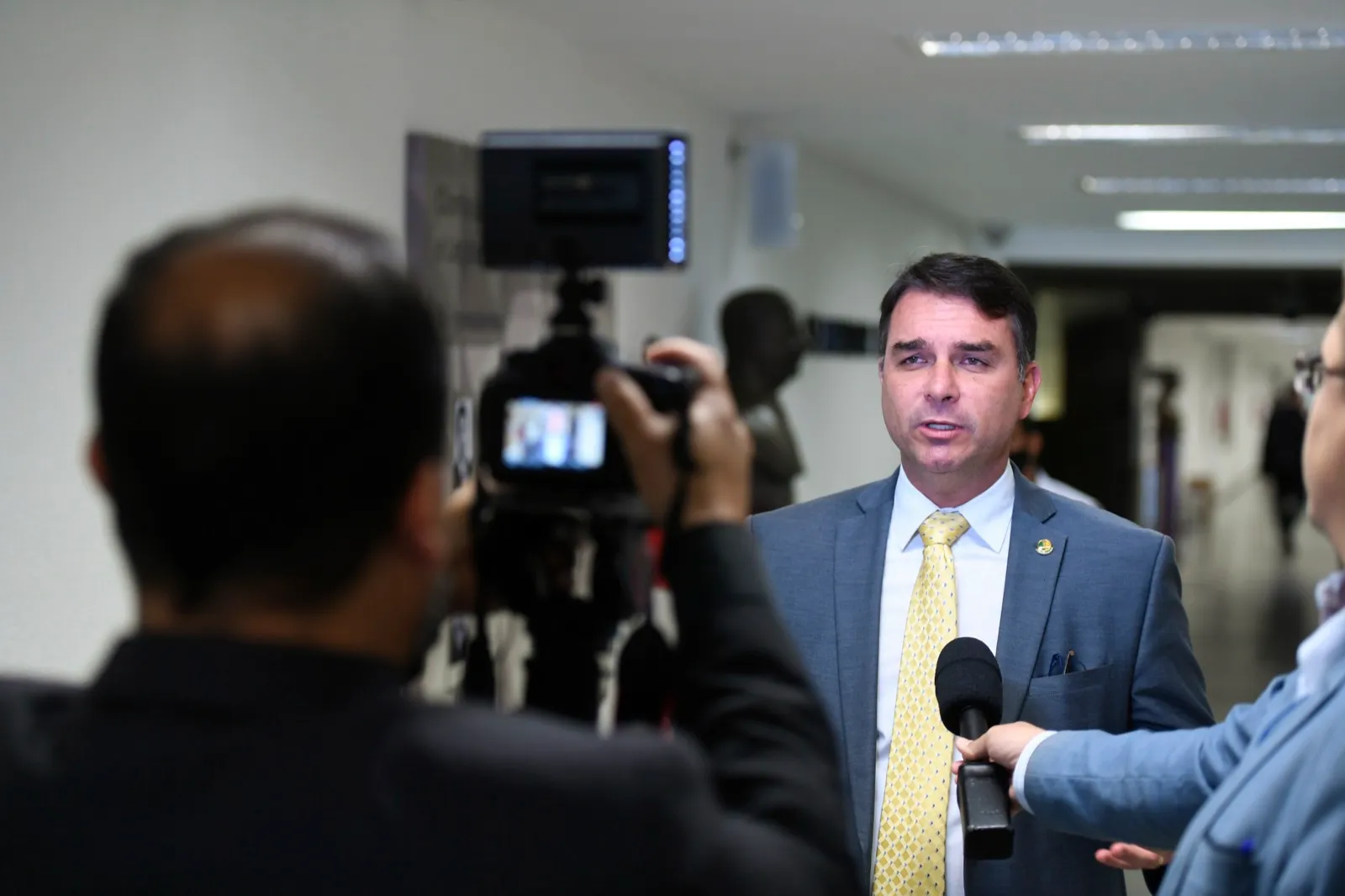 Flávio Bolsonaro fala a jornalistas, com câmera e microfone à sua frente, no Senado