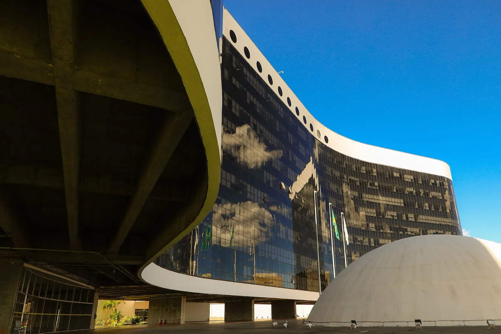 Fachada curva de vidro escuro do prédio do Tribunal Superior Eleitoral, em Brasília, sob céu azul.