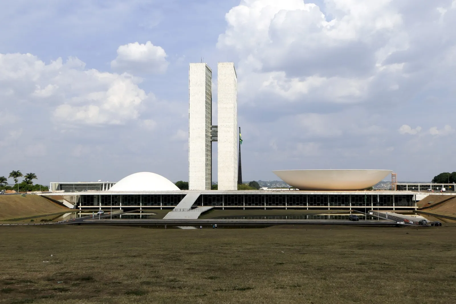 Fachada do Palácio do Congresso Nacional, com as duas torres e as cúpulas da Câmara e do Senado, sob céu claro com nuvens.